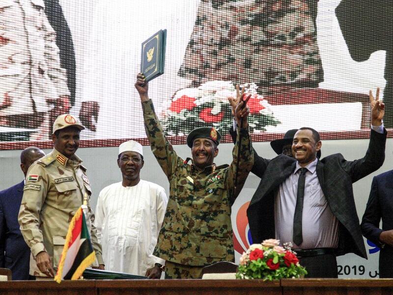In this file photo taken on August 17, 2019, Sudan's protest leader Ahmad Rabie (2nd-R), flashes the victory gesture alongside General Abdel Fattah al-Burhan (C), the chief of Sudan's ruling Transitional Military Council (TMC), during a ceremony where they signed a "constitutional declaration" that paves the way for a transition to civilian rule, in the capital Khartoum, accompanied by General Mohamed Hamdan Daglo "Hemeti" (2nd-L), TMC deputy chief and commander of the Rapid Support Forces (RSF) paramilitar