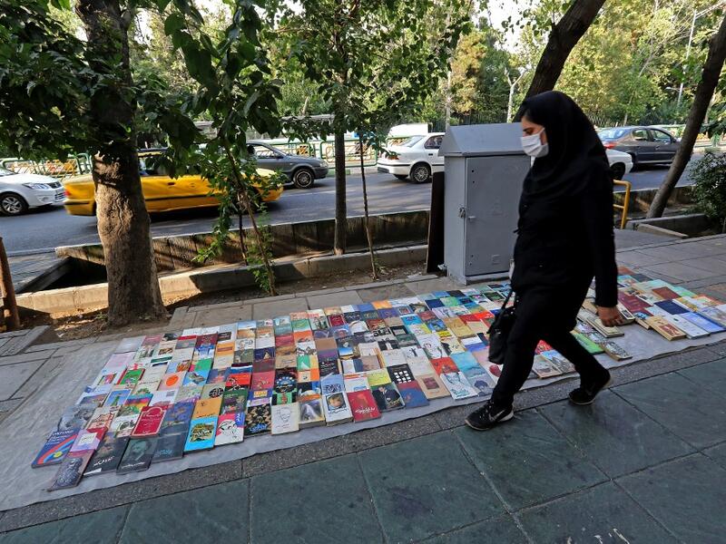 A woman walks past books displayed for sale along a pavement on Enqelab (Revolution) street in Iran's capital Tehran, on September 8, 2020. ATTA KENARE / AFP