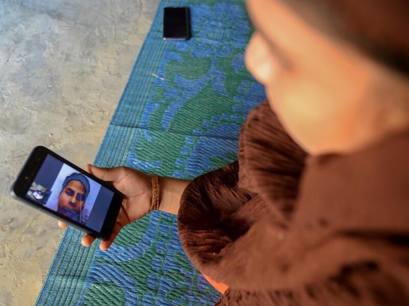 In this photograph taken on October 13, 2020, Rohingya refugee Umme Khair, who gave money to a community leader to travel to Malaysia to her husband, interacts with her spouse via video call at a makeshift shelter in Kutupalong Rohingya refugee in Ukhia. Stay in a squalid refugee camp -- hopeless, starving, and made to feel a burden -- or leave, risking death, rape, human trafficking and months at sea to reach a husband you've never met. This is the bleak choice many Rohingya women, already scarred from fle