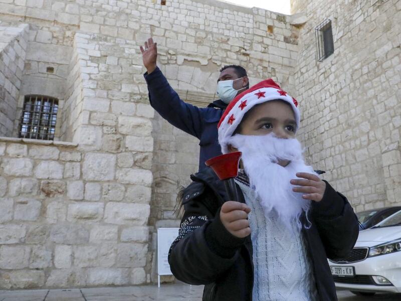 A Palestinian wearing a Santa Claus beard and hat rings a bell outside the Church of the Nativity, in the West Bank city of Bethlehem, on December 20, 2020 after it was re-opened for prayers following strict COVID-19 restrictions. HAZEM BADER / AFP
