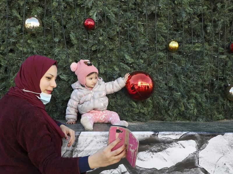 A Palestinian mother takes a picture of her daughter under a Christmas tree near the Church of the Nativity, in the West Bank city of Bethlehem on December 21, 2020. HAZEM BADER / AFP