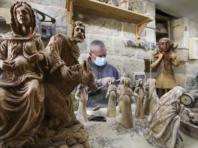 A Palestinian carpenter carves religious statues and figurines from olive wood at a shop near the Church of the Nativity, in the West Bank city of Bethlehem on December 21, 2020. HAZEM BADER / AFP