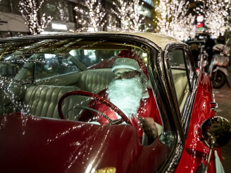 Rob Holtzapfel, a member of a vintage car group dressed as Santa Claus, sits in a 1959 Cadillac along a street lined with Christmas-themed light decorations in Marunouchi district in Tokyo on December 25, 2020. Philip FONG / AFP