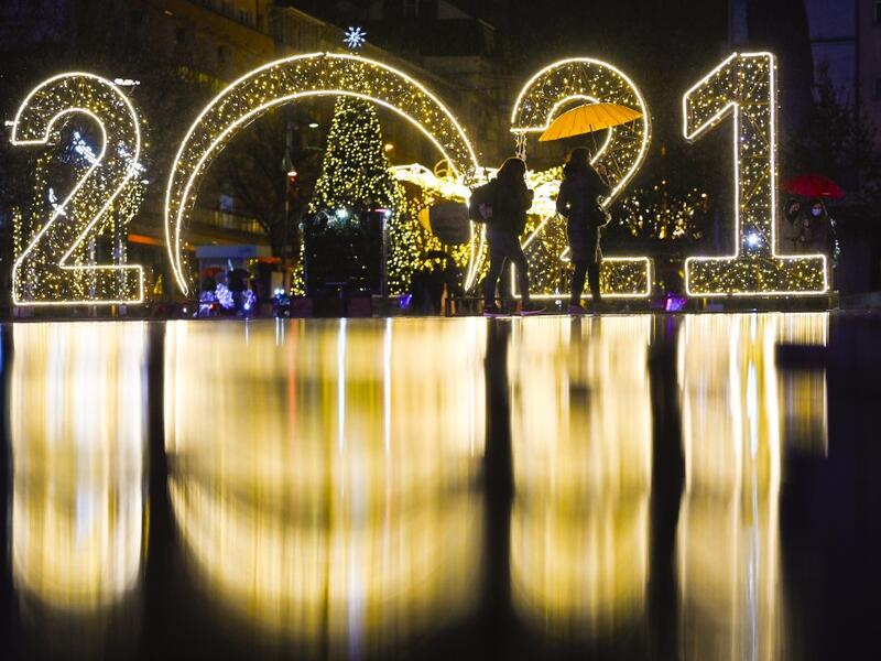 Women walk under an umbrella in front of a 2021 sign displayed in downtown Pristina on December 30, 2020, as Kosovars prepare to celebrate the New Year 2021 at their homes, amid the ongoing Covid-19 (novel coronavirus) pandemic. Armend NIMANI / AFP