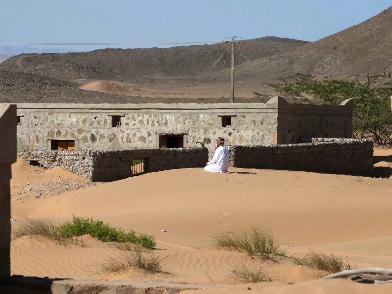 Mohammed al-Ghanbousi, a former inhabitant of Wadi al-Murr, kneels to pray on a sand dune among abandoned houses in the Omani village, about 400 kms (250 miles) southwest of the capital Muscat, on December 31, 2020. MOHAMMED MAHJOUB / AFP