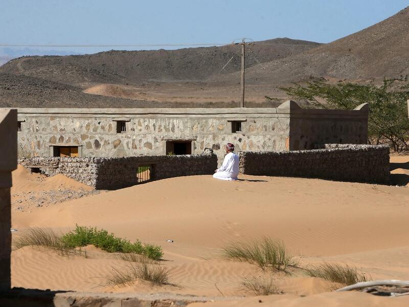 Mohammed al-Ghanbousi, a former inhabitant of Wadi al-Murr, kneels to pray on a sand dune among abandoned houses in the Omani village, about 400 kms (250 miles) southwest of the capital Muscat, on December 31, 2020. MOHAMMED MAHJOUB / AFP