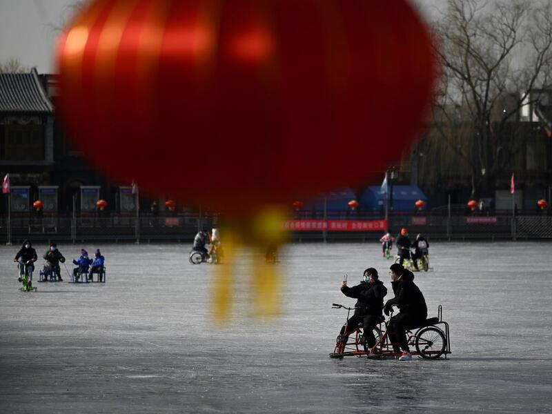 A man and a woman use a mobile phone to take a selfie as they ride sled on a frozen lake in Beijing on January 12, 2021. WANG Zhao / AFP
