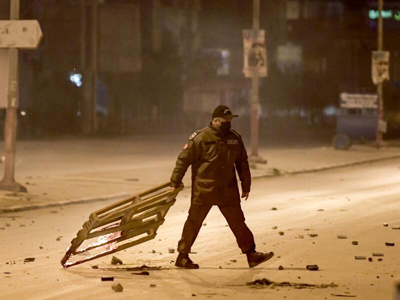 A member of Tunisia's National Guard drags a burning wooden mesh during clashes with protesters in the Ettadhamen city suburb on the northwestwern outskirts of Tunisia's capital Tunis on January 17, 2021, amidst a wave of nightly protests in the North African country. FETHI BELAID / AFP