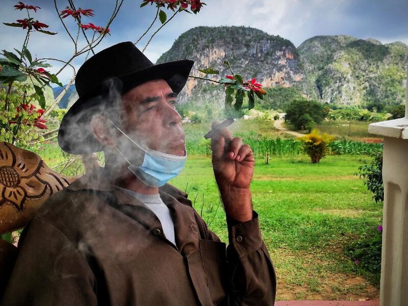 Eduardo Hernandez, owner of a private restaurant and a tobacco cultivator, smokes a cigar in his house in Vinales, Cuba, on January 28, 2021. At the foot of the majestic rock formations of Vinales, the terraces of the restaurants look empty and the lodgings have closed. With the arrival of COVID-19, the incipient prosperity of this Cuban town came to a halt and people abandoned tourism jobs to return to work the land. YAMIL LAGE / AFP