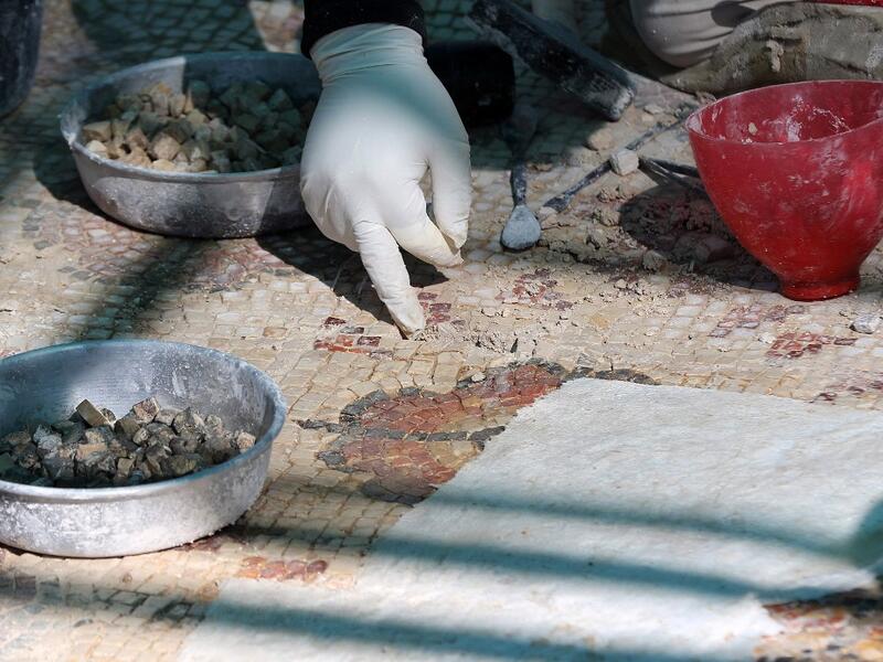 A worker employed by a pilot project run by the UN cultural agency UNESCO, restores a mosaic floor at an ancient church complex, in the small town of Rihab, some 70 kilometres north of the Jordanian capital Amman, on February 9, 2021. In the ruins of the ancient Byzantine church in Jordan, local townspeople and Syrian refugees work side by side on a project that unites preserving cultural heritage and fighting poverty.  Khalil MAZRAAWI / afp