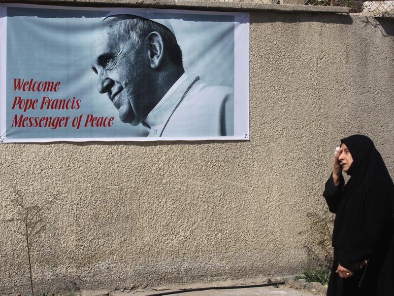 An Iraqi woman walks in front of a banner welcoming Pope Francis