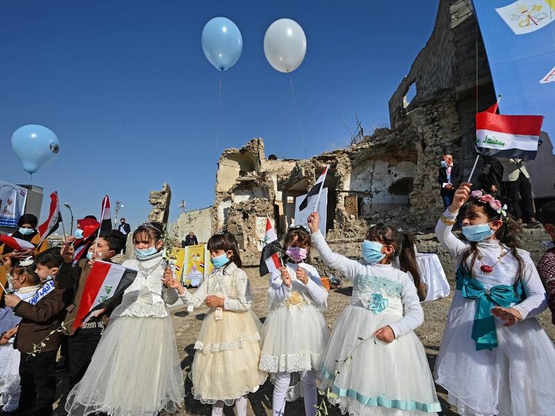 Iraqi children dressed in costumes wave national flags near the ruins of the Syriac Catholic Church 