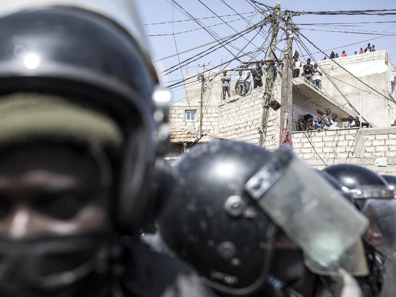 People gather on roofs to watch as police block supporters of main opposition candidate, Ousmane Sonko, outside the Justice Palace in Dakar on March 8, 2021. Protests have been ongoing after opposition leader Ousmane Sonko was arrested following rape charges. JOHN WESSELS / AFP