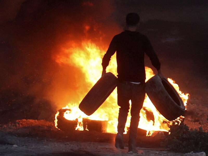 A Palestinian man sets a tire on fire in the village of Beita, south of Nablus, in the occupied West Bank, across the valley from the newly built Israeli settlers' outpost of Eviatar, on June 13, 2021. With flashing lasers, honking horns and choking smoke from burning tires, the latest tactics used by Palestinian protesters are dusk till dawn rallies to make life unbearable for Israeli settlers.