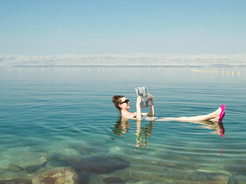 Girl reading newspaper floating on surface Dead Sea 