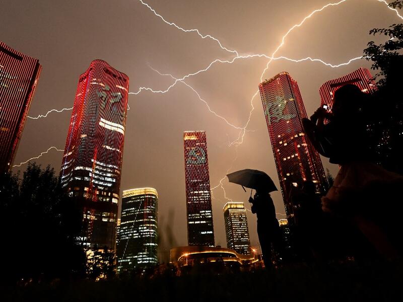 A bolt of lightning crosses the sky as people look at buildings displaying a light show on the eve of the 100th anniversary of the Chinese Communist Party in Beijing 