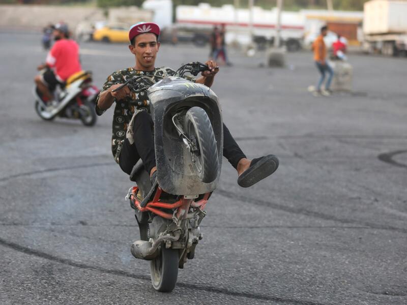 Iraqi youths perform stunts on their scooters in the Jadriya district of Baghdad on August 6, 2021. All dressed up and nowhere to go: many young Iraqis in Baghdad make an effort to be hip, even as they admit their country may have no future.