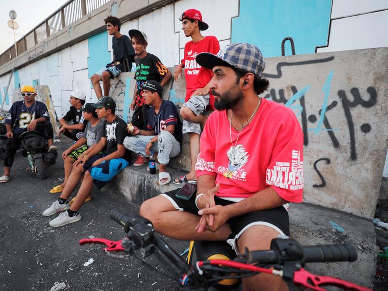 Iraqi youths watch others perform stunts on motorbikes and scooters in the Jadriya district of Baghdad on August 6, 2021. All dressed up and nowhere to go: many young Iraqis in Baghdad make an effort to be hip, even as they admit their country may have no future. 