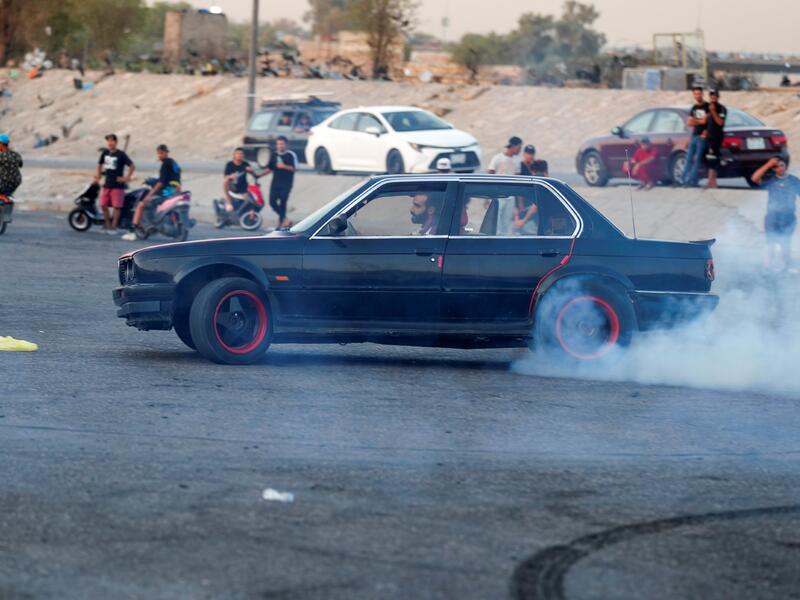 An Iraqi driver shows off his drifting skills as youths watch in the Jadriya district of Baghdad on August 6, 2021. All dressed up and nowhere to go: many young Iraqis in Baghdad make an effort to be hip, even as they admit their country may have no future. 