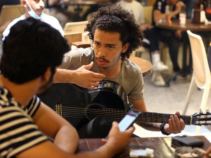 Iraqi guitarist Mohammed, 23, plays as he sits with his friends at a coffee shop in the Karrada district of the capital Baghdad, on August 6, 2021. All dressed up and nowhere to go: many young Iraqis in Baghdad make an effort to be hip, even as they admit their country may have no future. 