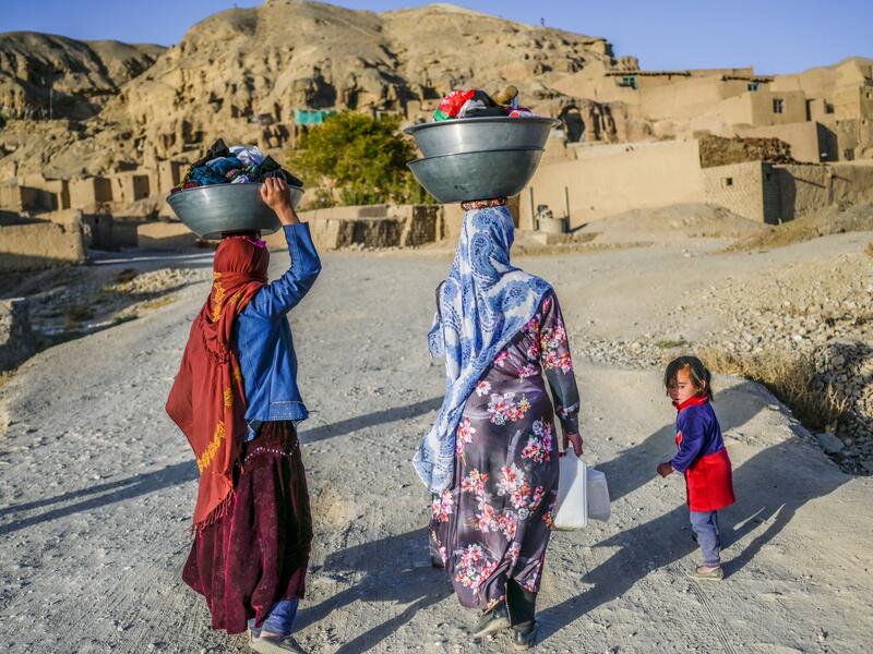 In this picture taken on October 3, 2021, Hazara ethnic women walk with their laundry to their village near the cliffs pockmarked by caves where people still live as they did centuries ago in Bamiyan. 