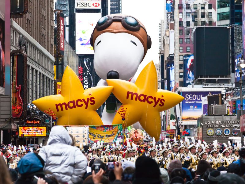 Snoopy balloon floats in the air during the annual Macy's Thanksgiving Day parade along Avenue of Americas with the Radio Music Hall in the background. (Gary 718/ Shutterstock)