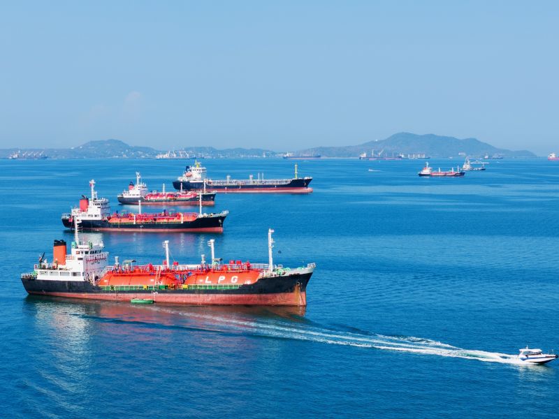 سفن ناقلات غاز البترول المسال والنفط راسية في المحيط، مع قارب دورية سريع في المقدمة. نقل الطاقة العالمي