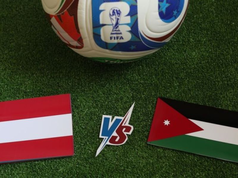 علم الأردن وعلم النمسا على أرضية ملعب كرة قدم مع كرة تحمل شعار كأس العالم قبل المباراة بين المنتخبين.