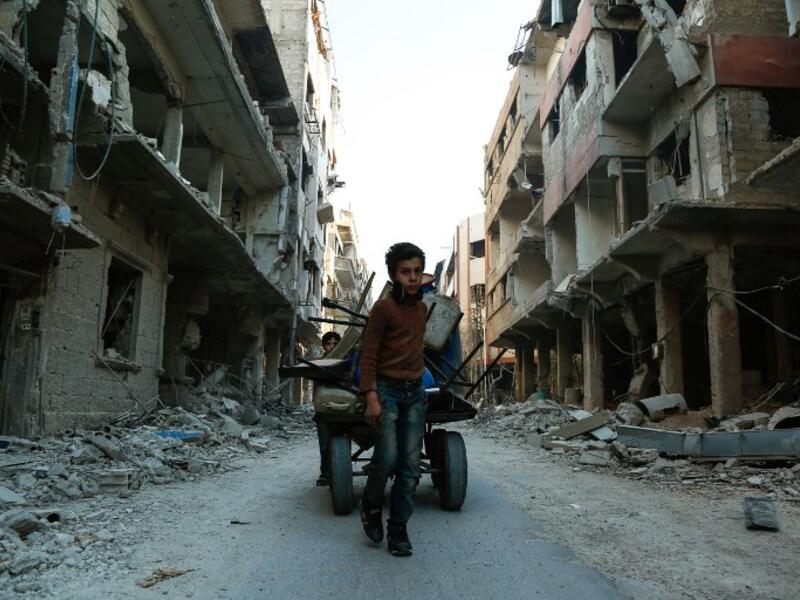 A Syrian boy pulls a cart with items collected amidst debris of destroyed buildings in Douma, in the rebel enclave of Eastern Ghouta on the outskirts of Damascus on Mar. 12, 2018. (HASAN MOHAMED / AFP)