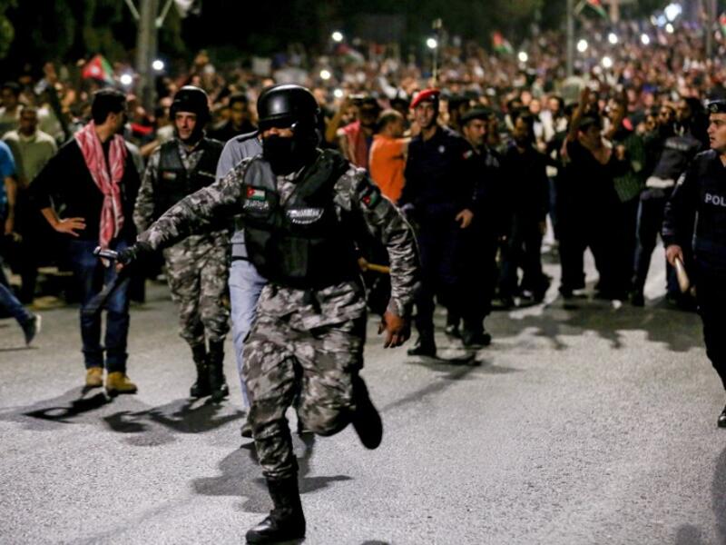 A member of the Jordanian gendarmerie runs as riot police stand on guard before protesters during a demonstration outside the Prime Minister's office in the capital Amman late on June 2, 2018. 
Khalil MAZRAAWI / AFP