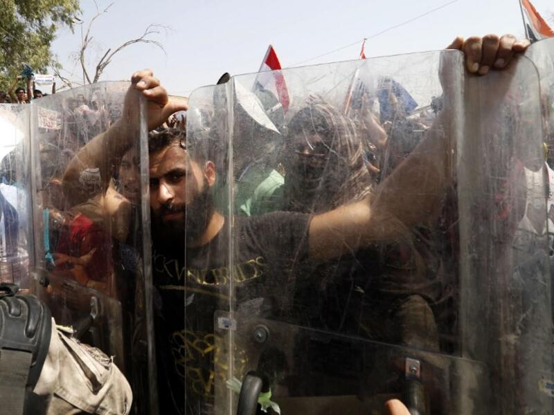 A protester grabs the shields of Iraqi security forces forming a human barrier, during a demonstration against unemployment and a lack of basic services, in the southern Iraqi city of Basra on July 15, 2018. (AFP/Haidar Mohammad Ali)