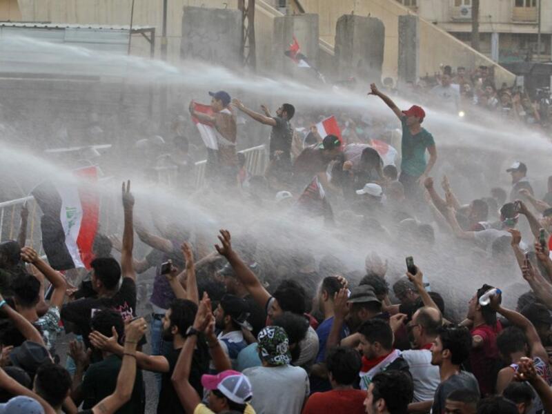 Iraqi protesters waving national flags are being sprayed with water cannon by security forces during a demonstration against unemployment and a lack of basic services in the capital Baghdad's Tahrir Square on July 20, 2018. (AFP/ Ahmad Al Rubaye)