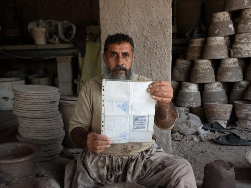 In this photo taken on October 10, 2018.Afghan potter Shirin Agha, 45, poses for a picture as he holds his id card or Tazkira registered to vote in the upcoming parliamentary election at his workshop, on the outskirts of Jalalabad. 
NOORULLAH SHIRZADA / AFP