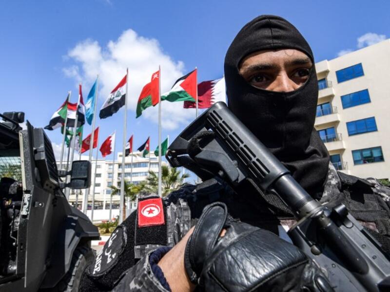 A member of the Rapid Intervention National Brigade (BNIR) of the Tunisian security forces standing guard by the national flags of the Arab League member states, outside Council of Arab Interior Ministers' headquarters, ahead of the Arab League summit due to take place in Tunis. 
FETHI BELAID / AFP