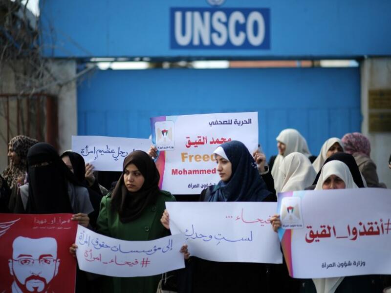 Palestinian women hold posters bearing a portrait of Palestinian hunger striking Palestinian journalist Mohammed al-Qiq on February 21, 2016. (AFP/Mahmud Hams)
