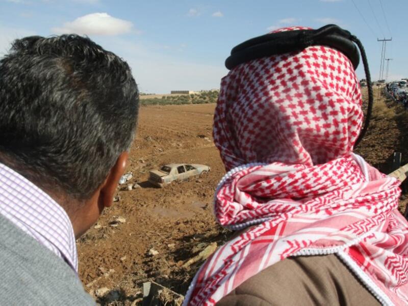 Jordanians stare at a car, submerged in mud following flash floods (AFP)