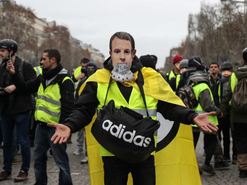 A protestor wearing a "yellow vest" (gilet jaune) and with a French President Emmanuel Macron mask poses on the Champs Elysees avenue in Paris (AFP)