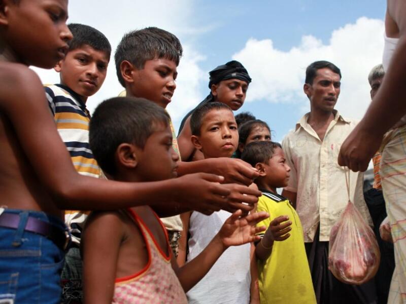 A Bangladeshi man distributes meat from a sacrificed animal to Rohingya refugees, during Eid al-Adha (AFP)