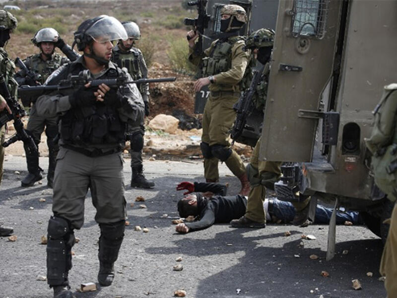 Israeli soldiers stand over an injured Palestinian man during clashes near Ramallah in the West Bank, October 7, 2015. (AFP/File)