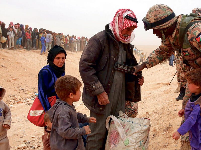 A Jordanian soldier scans newly arrived Syrian refugees as they wait to cross the border. (AFP/ File Photo)