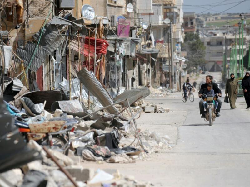 Civilians drive past damaged buildings in Maarat al-Numan, Syria. (AFP/File)
