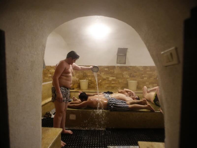 A man pours water on others lying on their bellies inside the steam room of the first traditional Turkish bath (Hammam) opening in the occupied Palestinian West Bank city of Hebron on March 11, 2019. 
HAZEM BADER / AFP