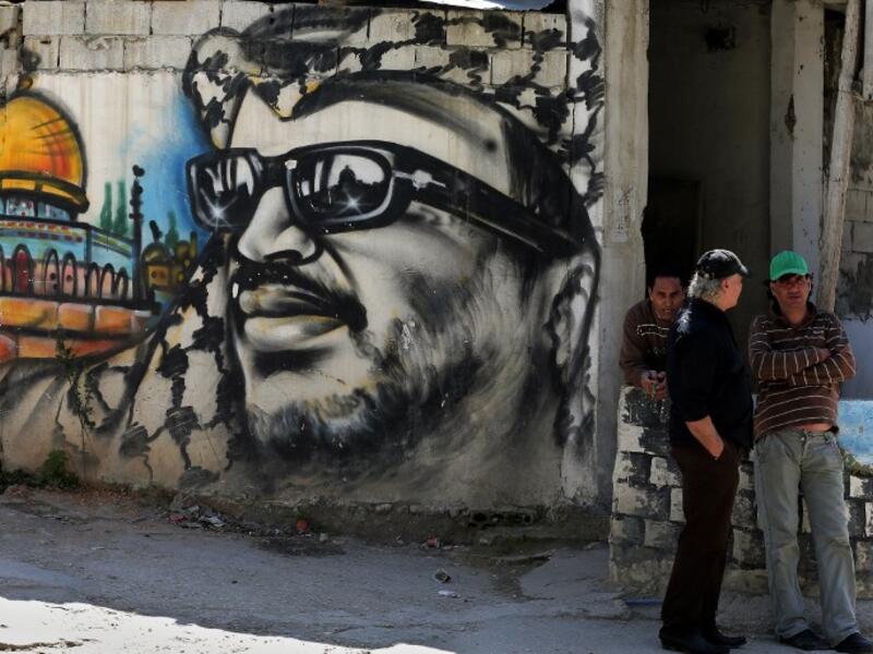 Palestinian refugees stand next to graffiti bearing a portrait of late Palestinian President Yasser Arafat at Ain el-Helweh camp in Lebanon. (AFP/File)