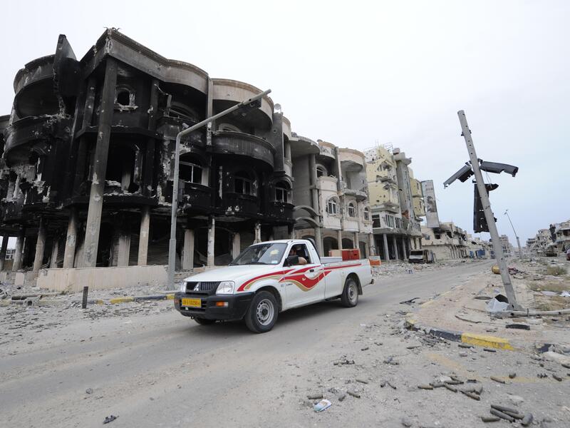 Libyans drive through a destroyed neighborhood in Sirte in 2011. (AFP/File)