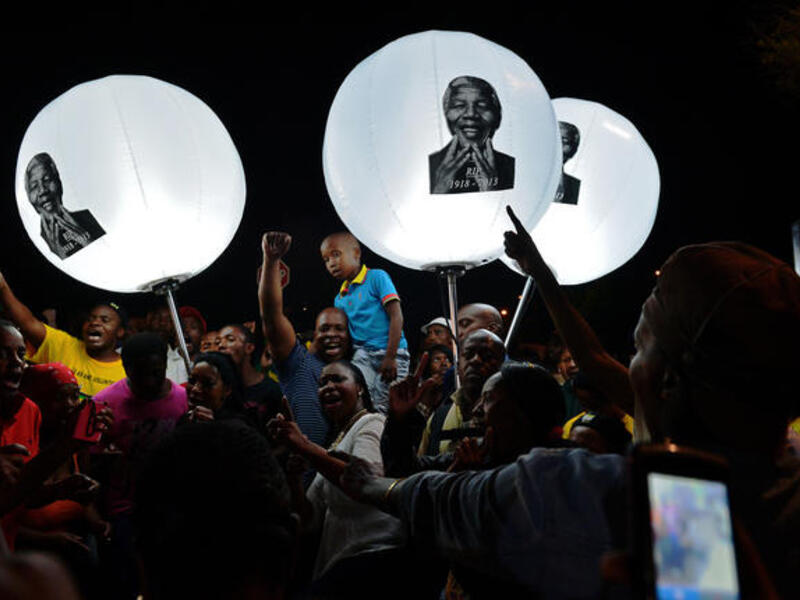 People hold up balloon lamps bearing the image of late former South African president Nelson Mandela during a commemorative ceremony outside the late leader's former home. [AFP]