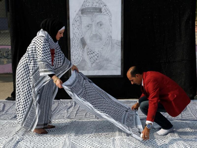 Palestinian Southern Education Direction's member Safa'a Amro (L) prepares a one thousand four hundred Meter square Keffiyeh (named "Arafatian" after the late Palestinian leader) to apply for the Guinness book of World Records' largest Keffiyeh in dura. (HAZEM BADER / AFP)