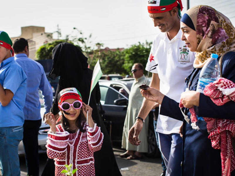 A young Jordanian girl, wearing a dress made out of a traditional kuffiyeh, tries on her pink sunglasses as she and her parents head to the festival.