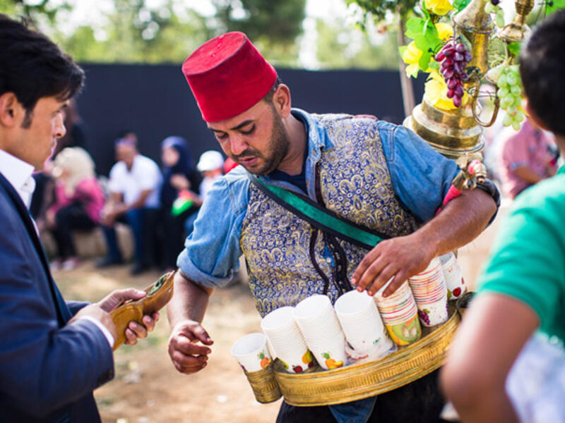 A Jordanian man wearing an Ottoman-style vest and fez, pours iced hibiscus juice for thirsty festival-goers at King Hussein Park on the centennial of the Great Arab Revolt on June 3, 2016.