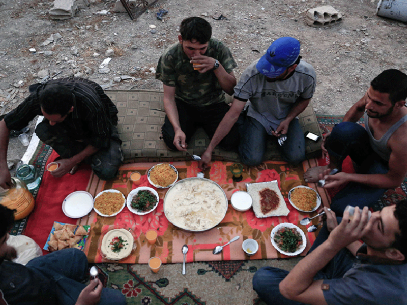 Fighters from the Syrian army gather for a simple Iftar dinner. Inflation and extremely high food prices have made it costly for many people to afford Iftar meals. Often, families cannot afford dates and milk to break their fast. Many also live without the traditional sweets, due to the skyrocketing prices for sugar. 