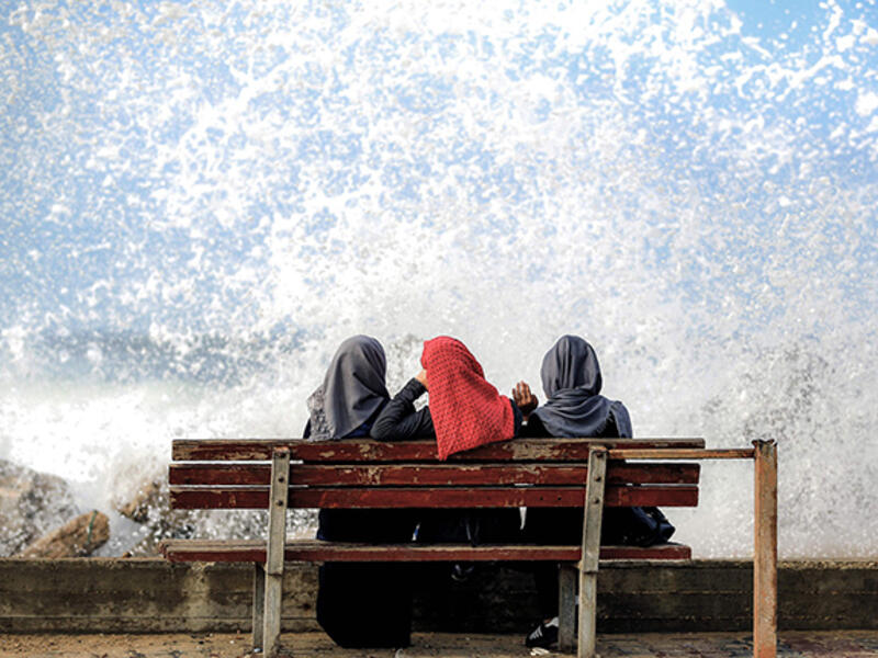 Three Palestinian women sit in the spray from the sea in Gaza City. 
